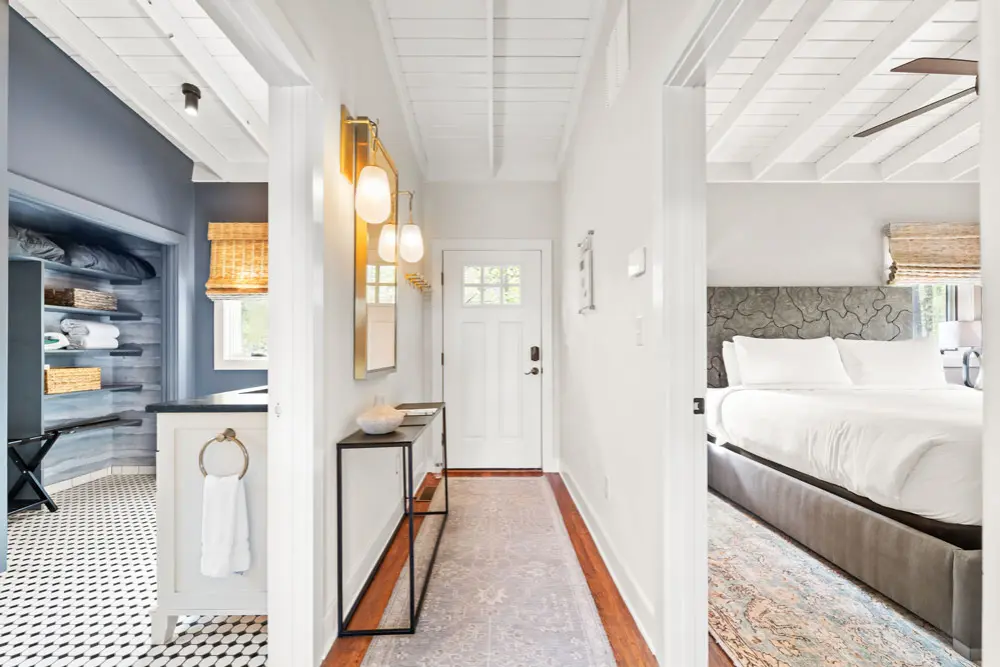 Hallway with white walls, and a view into a bedroom and bathroom.