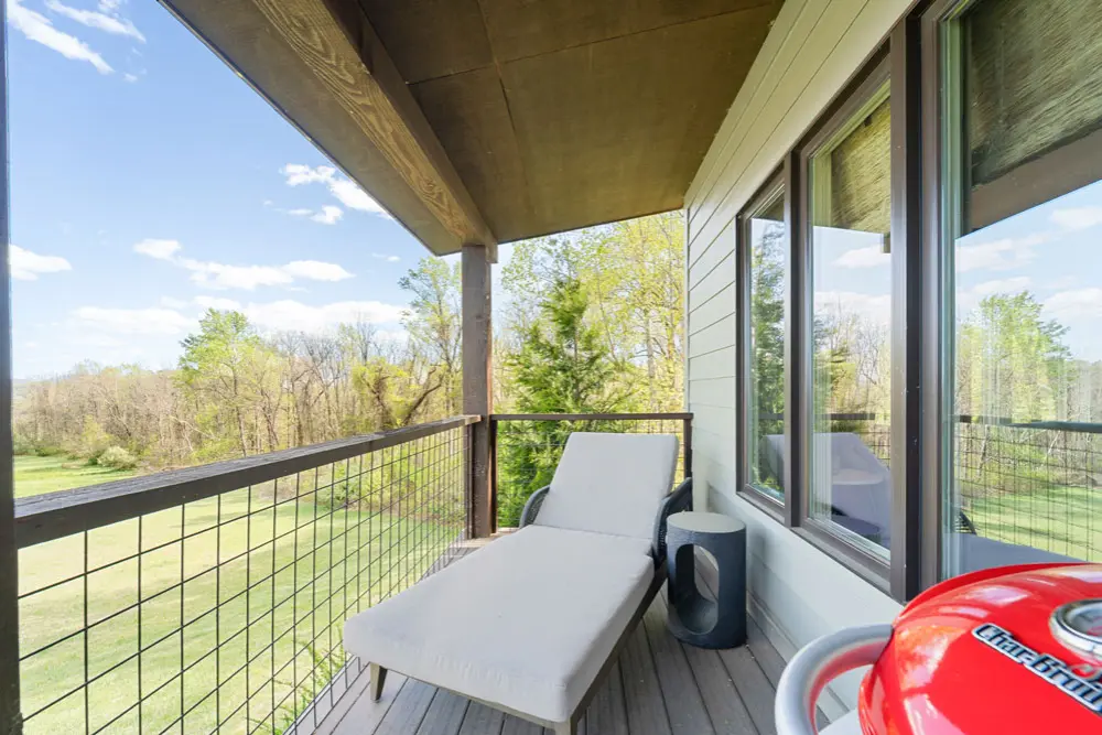 Outdoor deck with lounge chair, grill, and scenic view.
