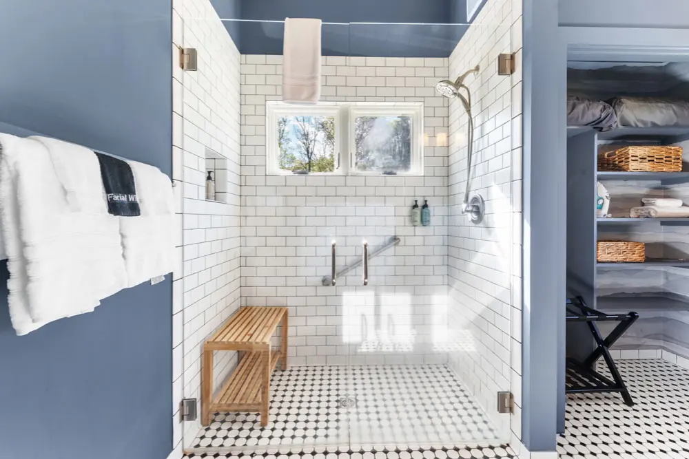 Shower with subway tile, glass enclosure, and wooden bench.