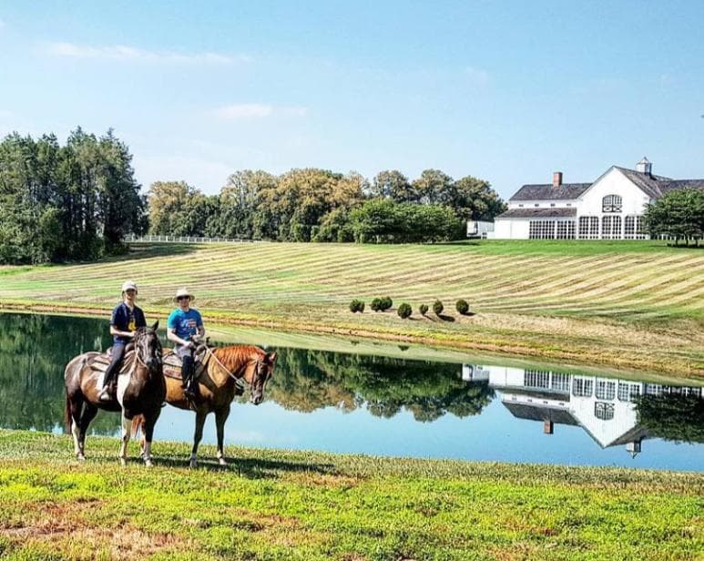Two woman riding a horse with a lake in the background.