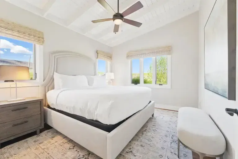 Bedroom featuring a king-sized bed, ceiling fan, and large windows.
