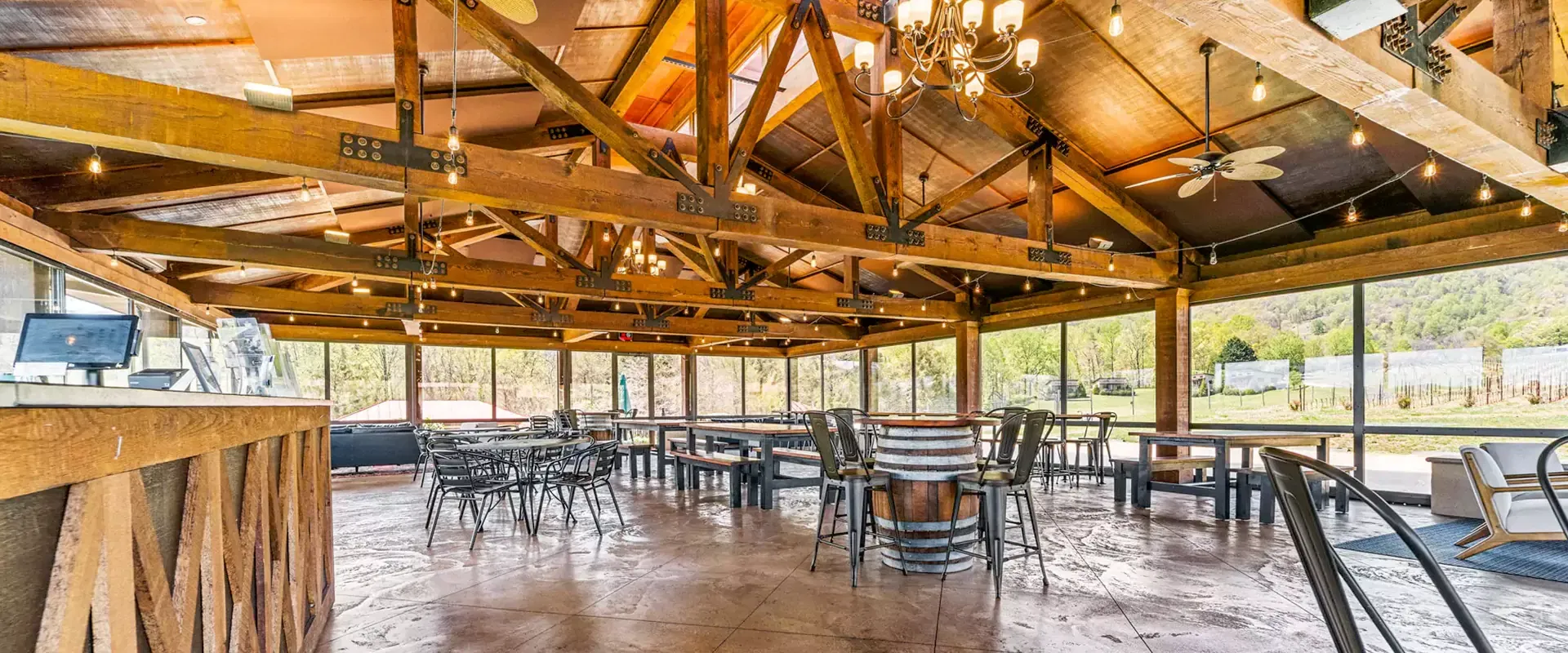 Winery tasting room with wooden beams, metal chairs, and vineyard views.