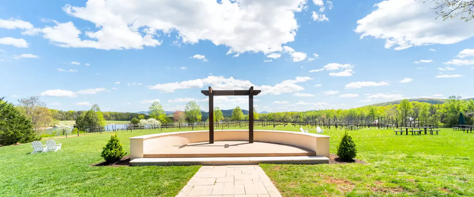 Stone path leading to a wooden arch overlooking a lake under a bright blue sky.