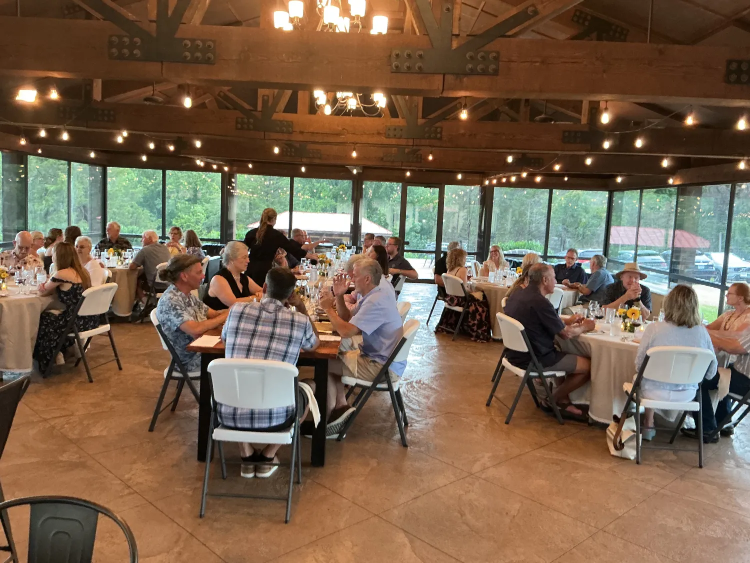 Guests seated and dining together inside a vineyard pavilion, enjoying a communal meal in a warm, rustic setting with scenic outdoor views.